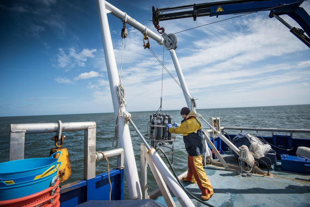 Scientist lowering sea water sampling experiment into sea on research ship